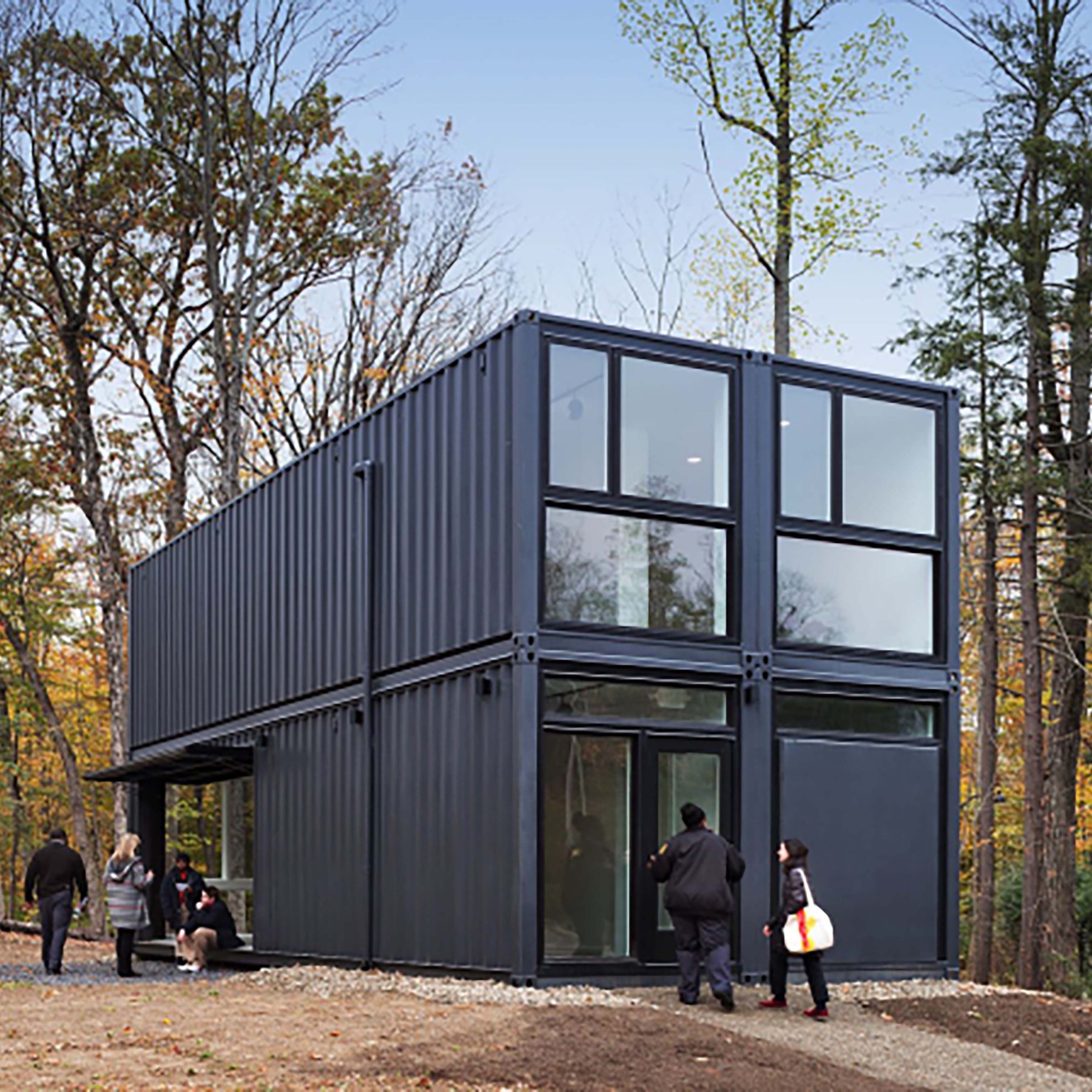 Black revamped, modern shipping container in forest with people around