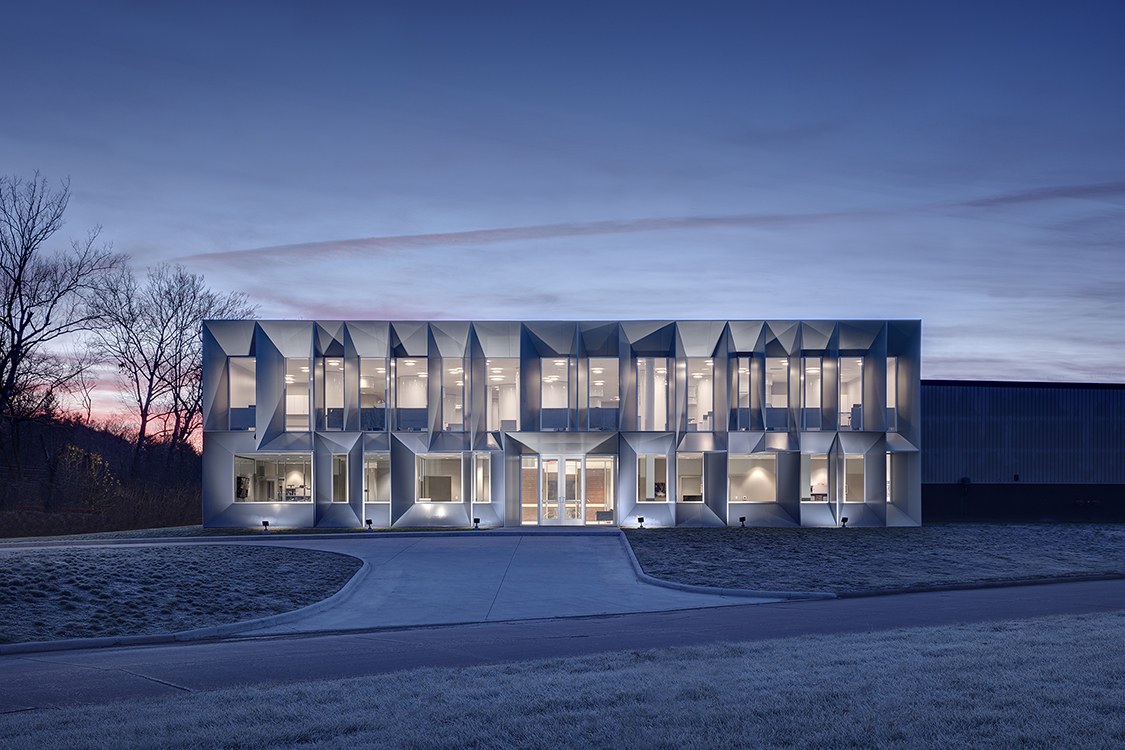 Night photo of a work by MPdL Studio of a modern two-story rectangular building with interior lights flooding out of floor-to-ceiling windows.