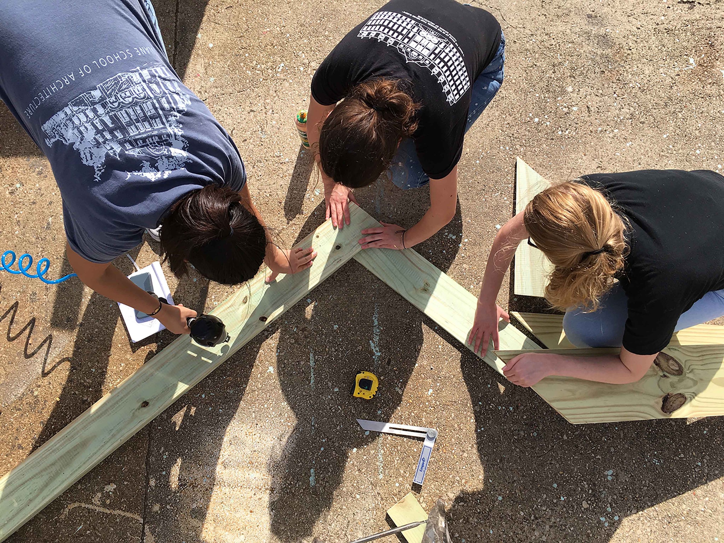 Three girls working on construction project, aligning wood beams 