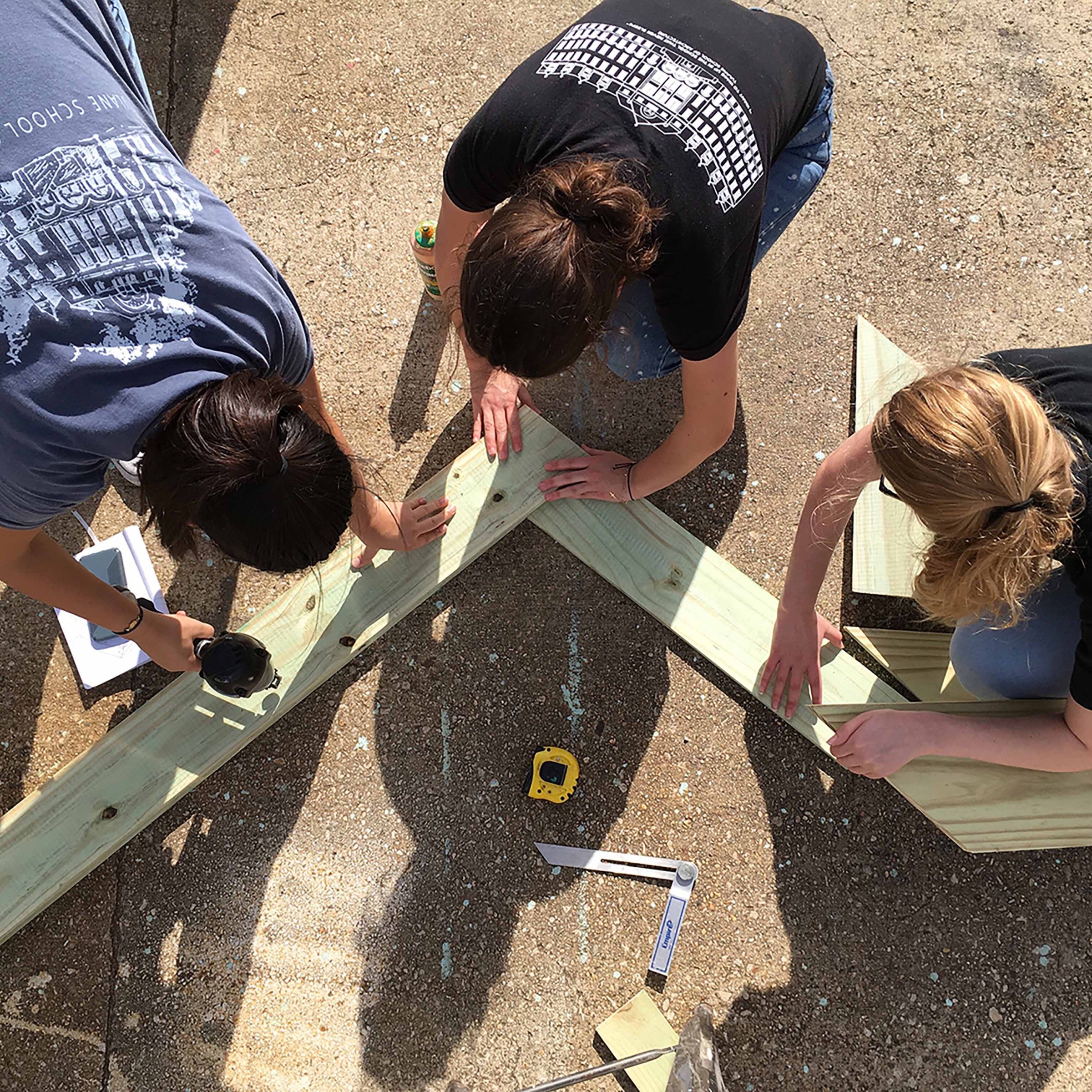 Three girls working on construction project, aligning wood beams 