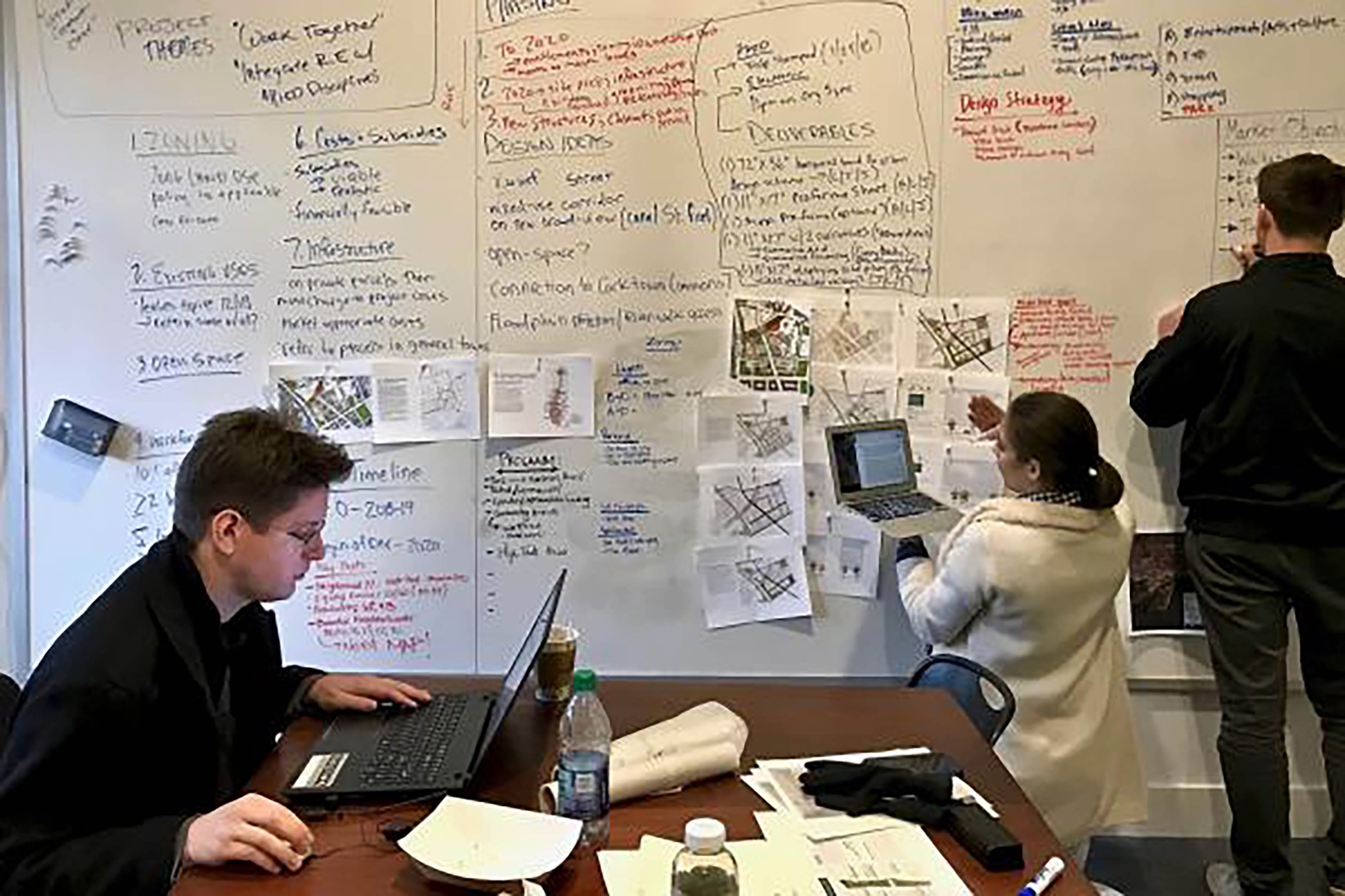 Three students working collaboratively on computers and writing on whiteboard