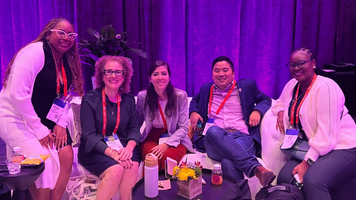 Five students sitting, smiling and looking at camera in a dark room at a social networking event.