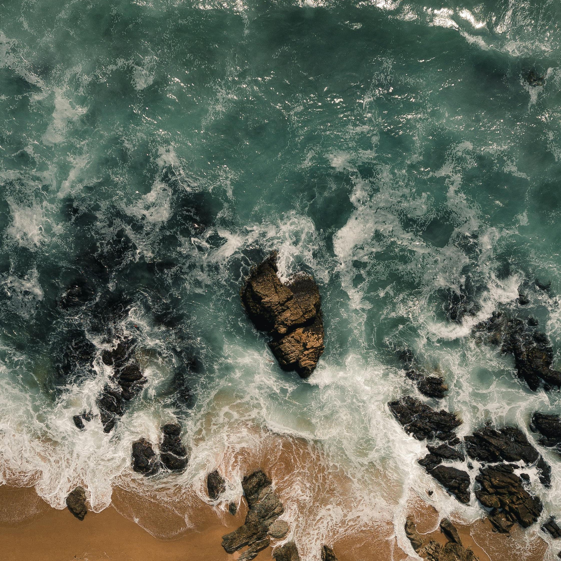 Aerial view of waves on beach with rocks and sand.