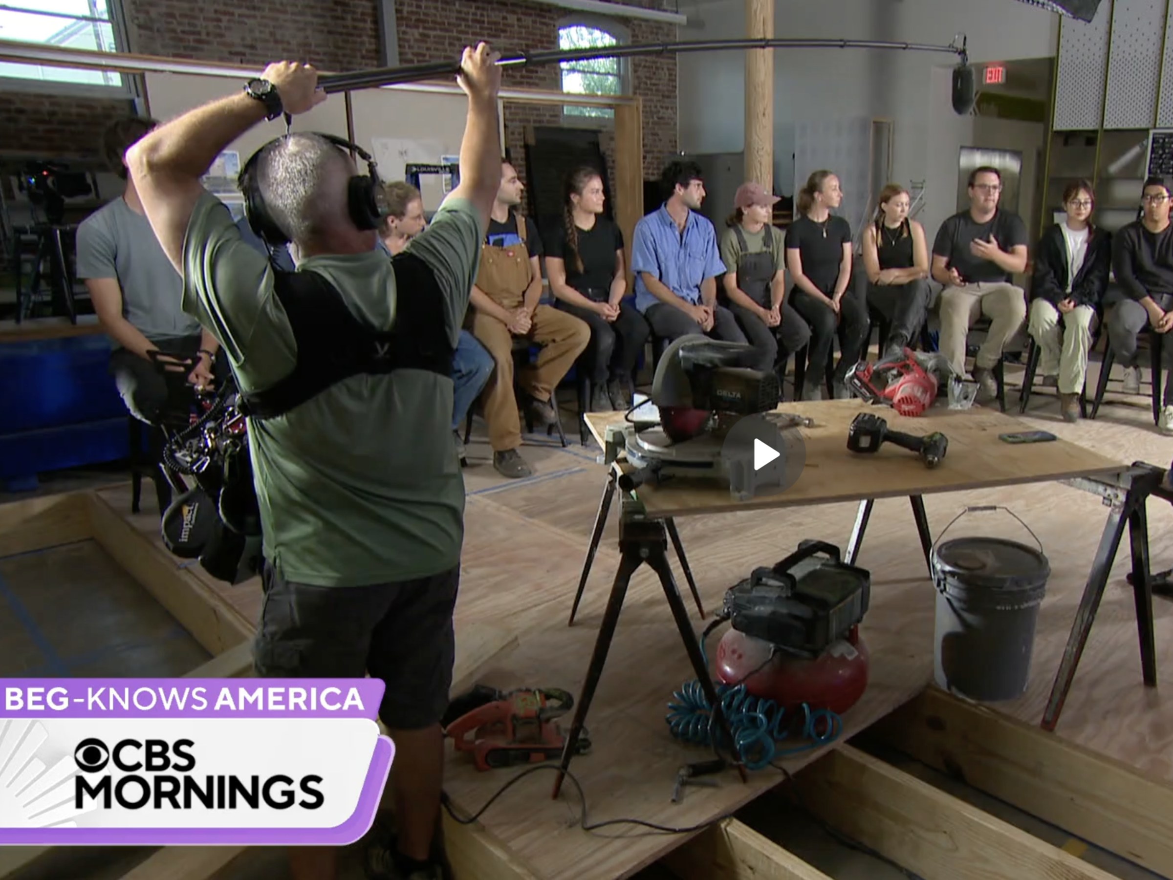 Screenshot of CBS News video of students sitting inside a large workroom with a boom mic operator in the left-side of the screen.