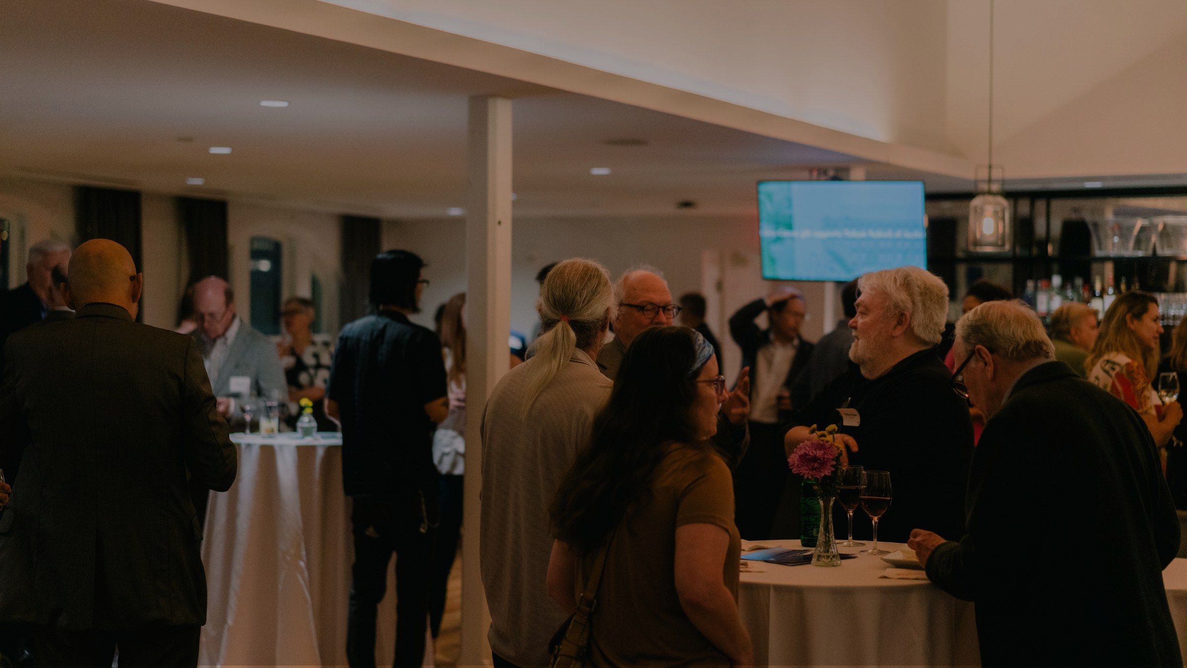 People talking while standing around small tables at an inside reception event for alumni.