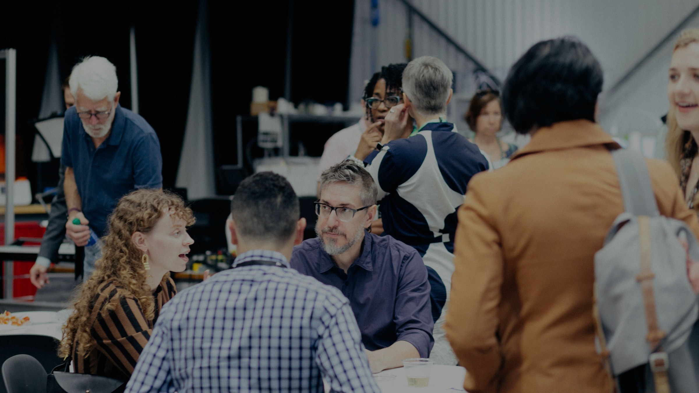 People talking while standing and sitting at small tables at an inside event for alumni.