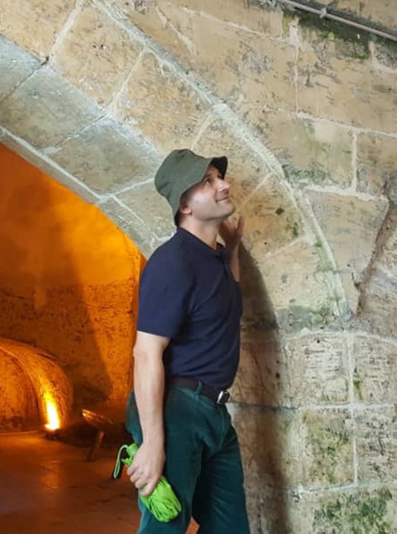 Eisa Esfanjary stands next to a stone archway, looking up toward the ceiling.