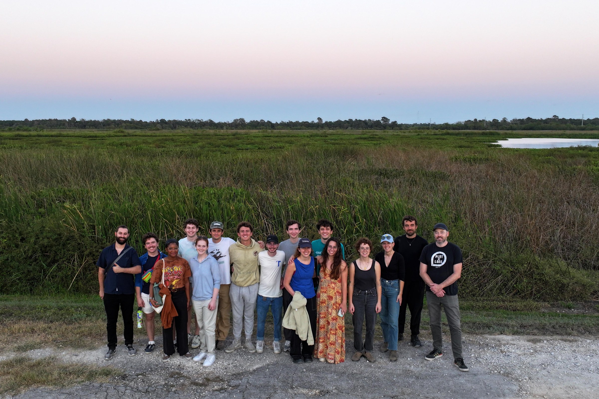 A group of people posing in front of tall grassy land. 