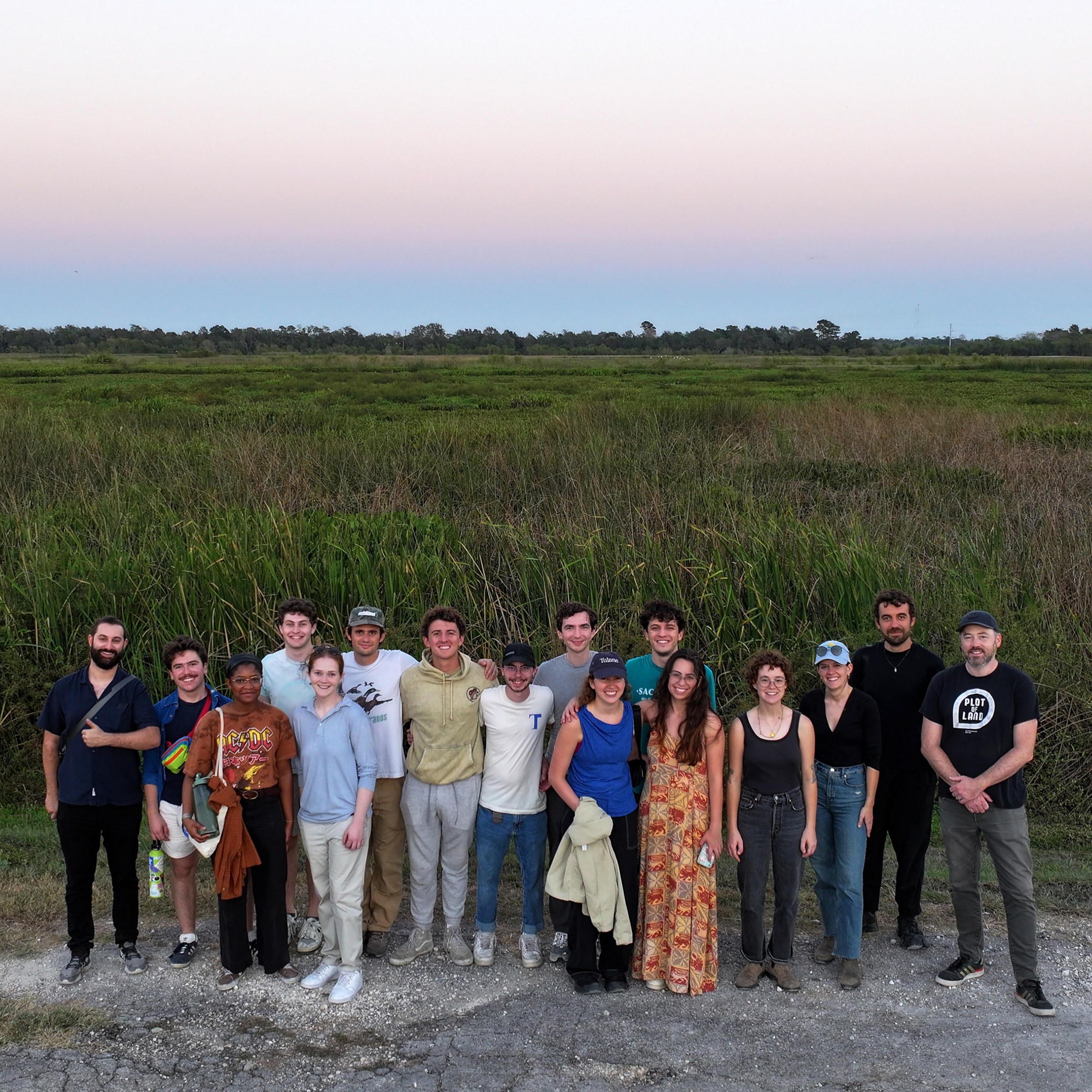 A group of people posing in front of tall grassy land. 