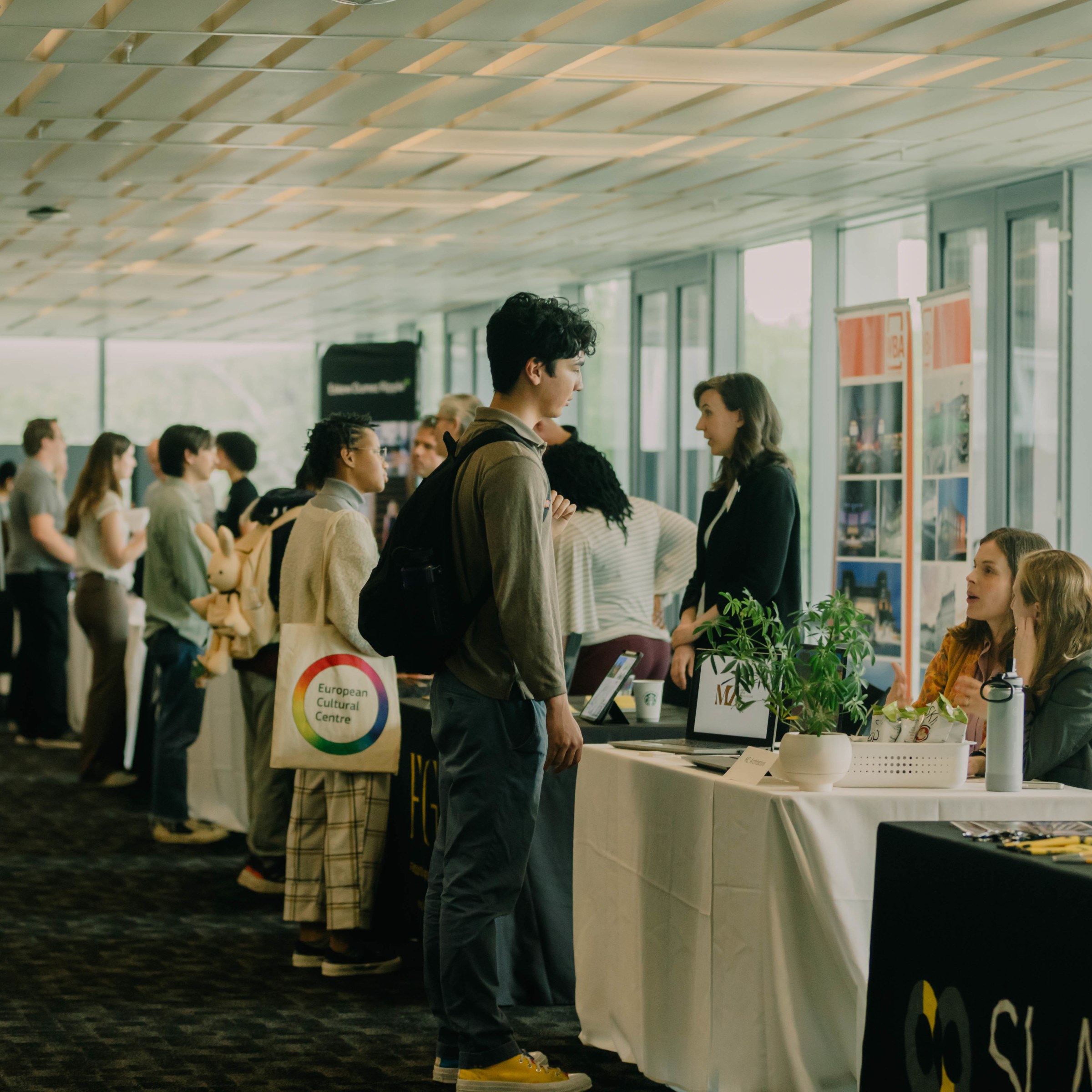 Several students stand facing a long line of tables with potential employers sitting and standing on the side of the tables, engaged in conversation with the students.