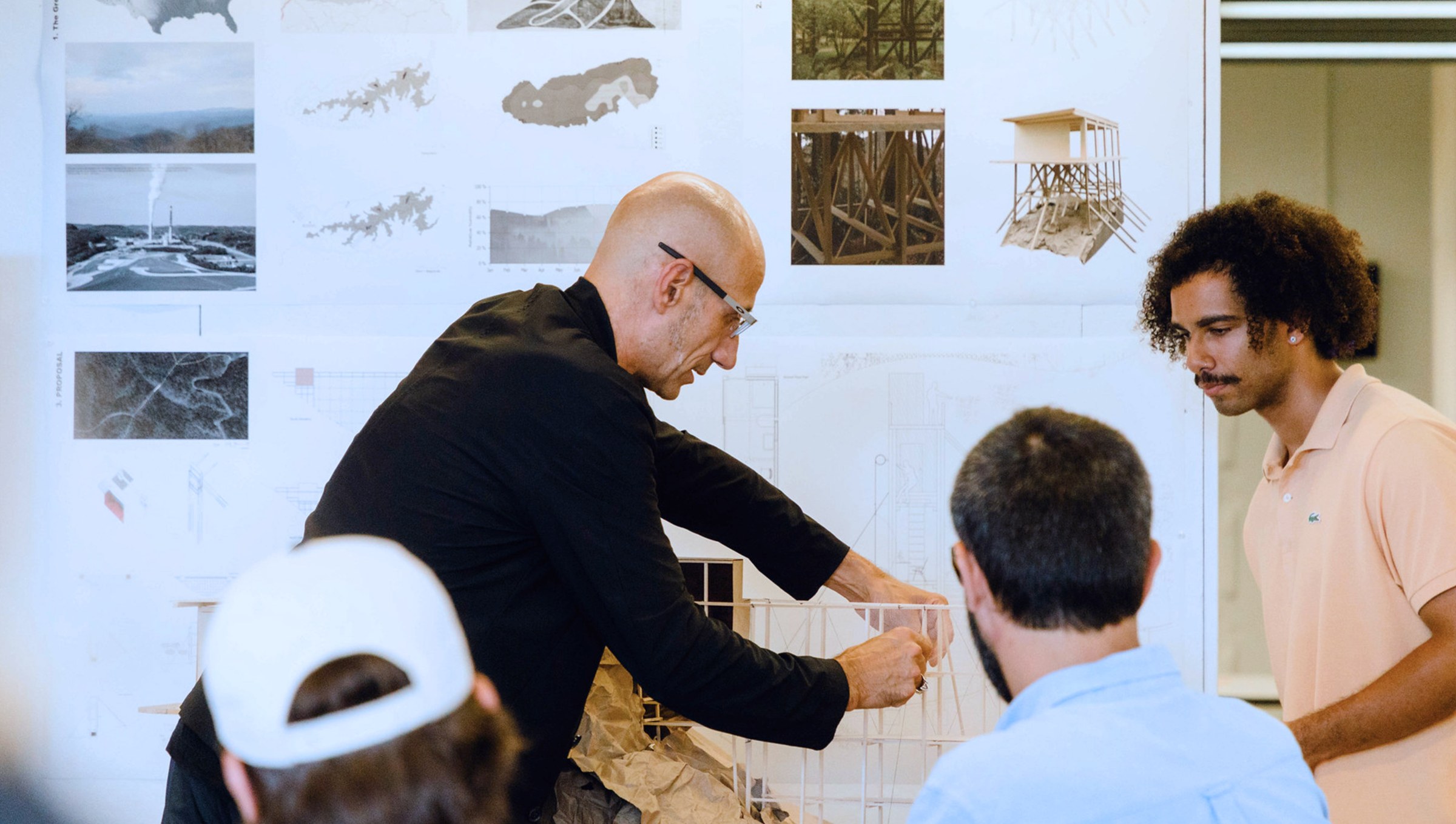 A faculty member and student are inspecting a physical model, while standing in front of a pinup board in the background.