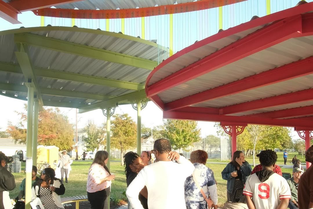 Lots of people stand and talk under the three-part circular metal roof of the Sprout House shade pavilion.