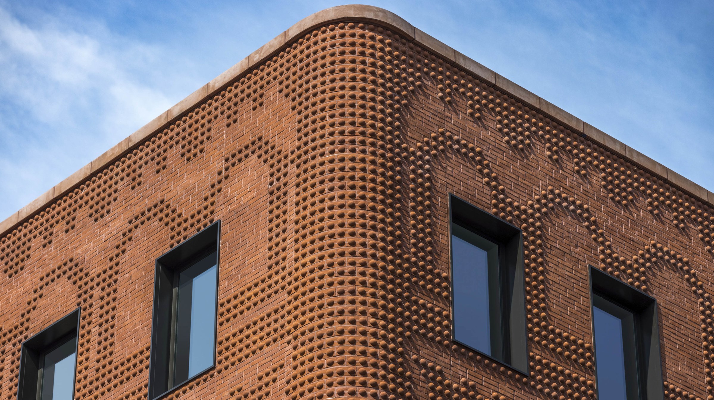 Close-up view looking up at a corner of a brick building with sky above, emphasizing the unique brick pattern.
