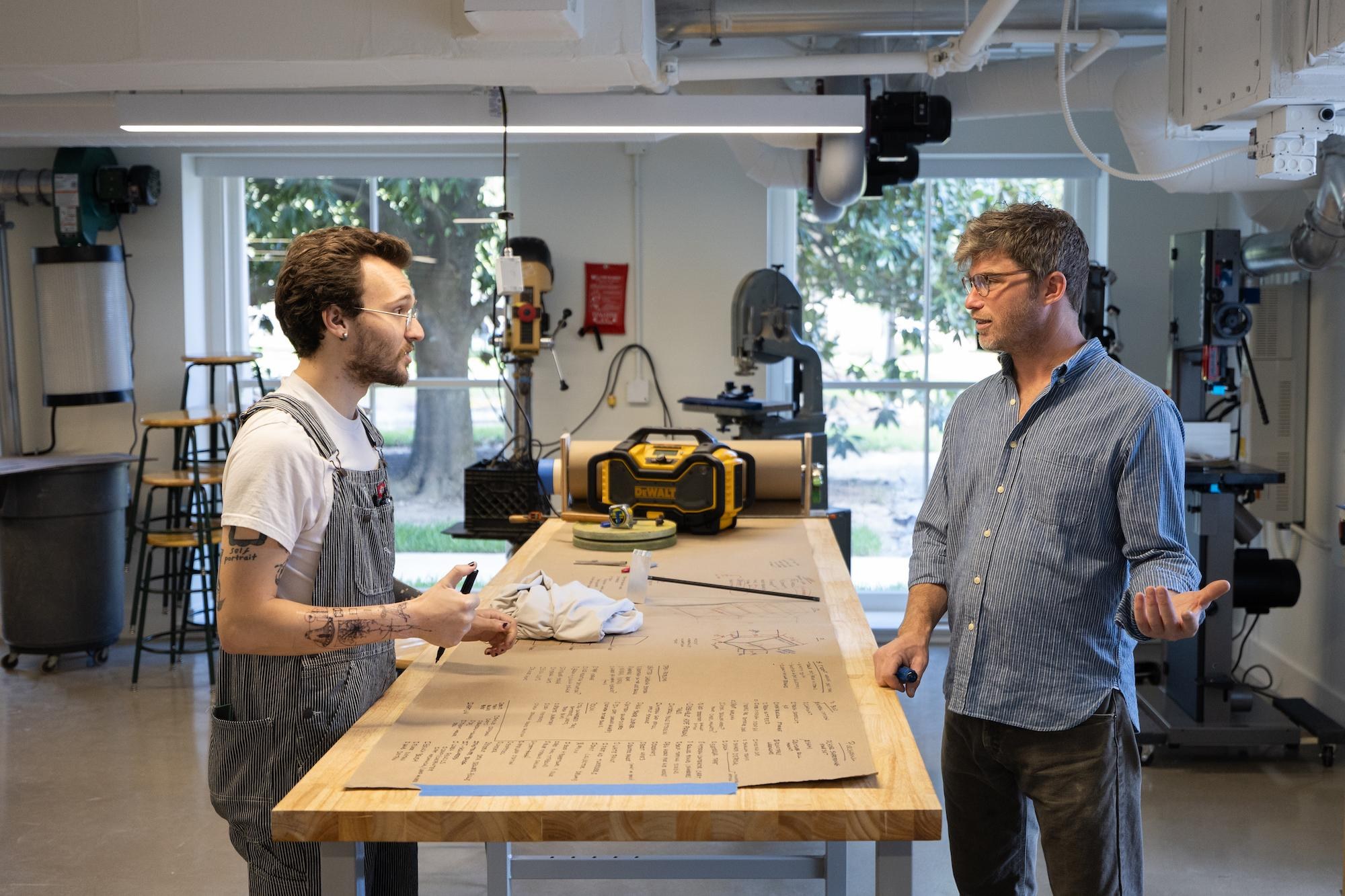 jesse and nick standing in front of a table in the woodshop