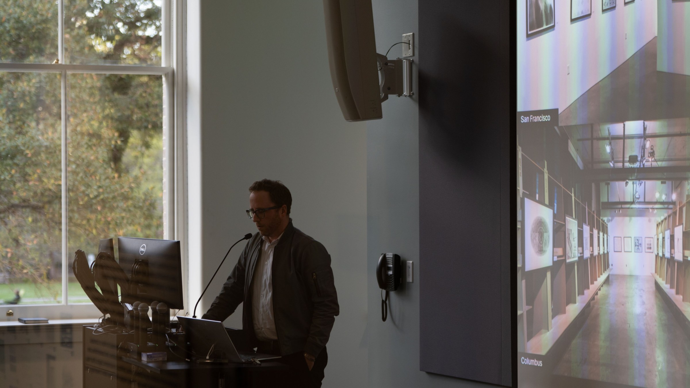 Angled view of a faculty presenting at a podium in front of a projector screen.