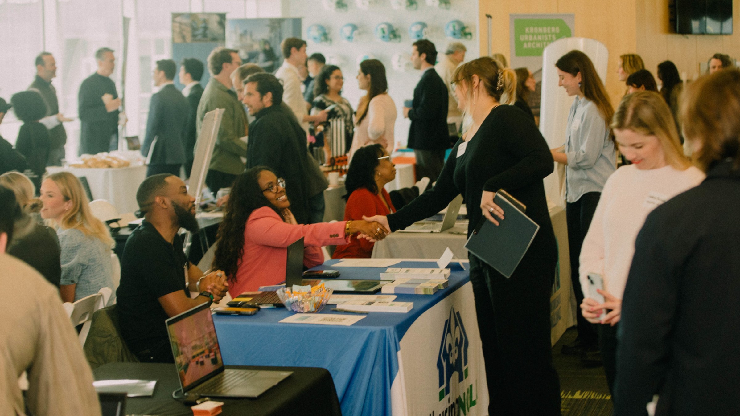 Wide shot of a career expo event in a large room with employers at tables and students talking to a shaking hands with employers.