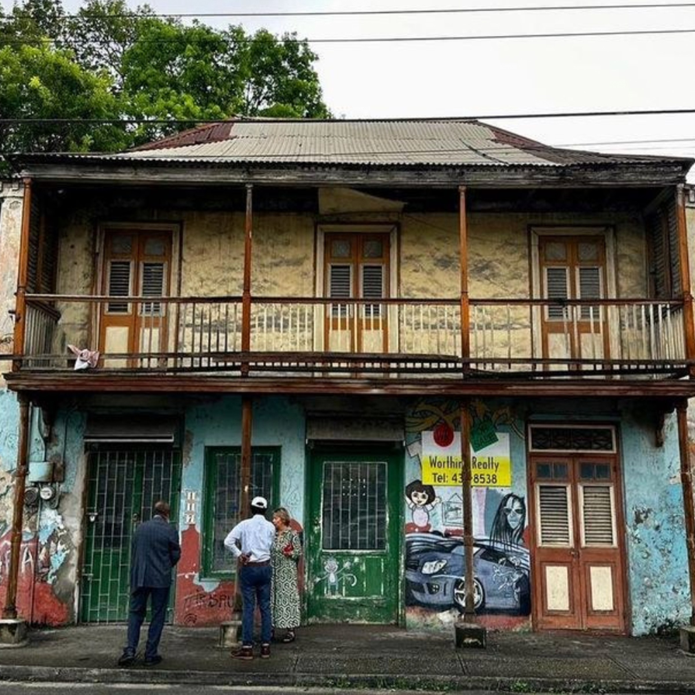 exterior of a two-story building with a balcony with graffiti or art on the first floor the building in need of preservation