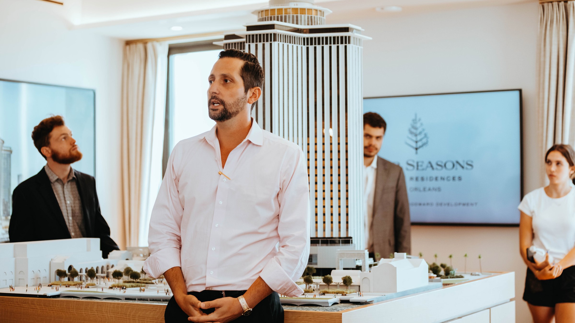 Photo of someone speaking in front of a group in an open room with a large hotel model in the background.