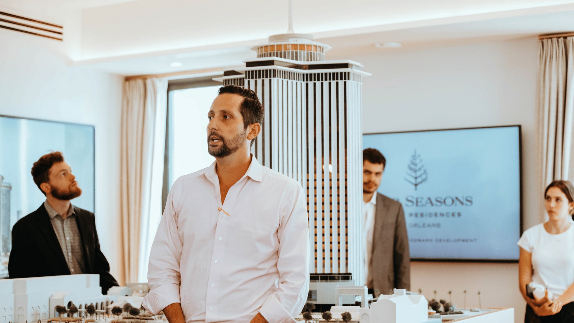 image of someone speaking in front of a group in an open room with a large hotel model in the background.