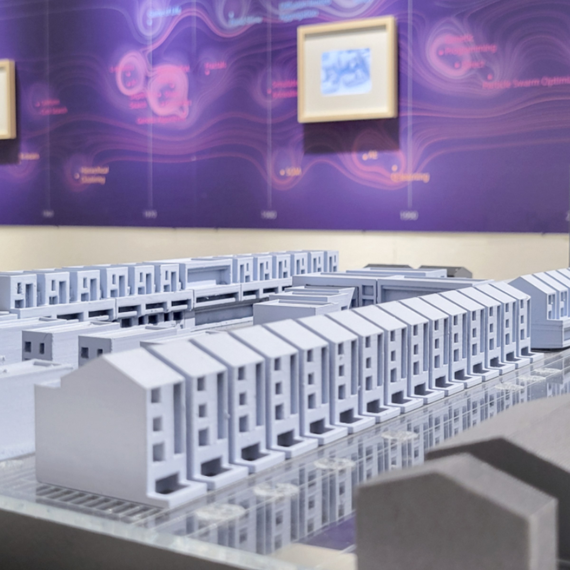 Model of rows of white buildings with a purple presentation poster and display on the wall behind it